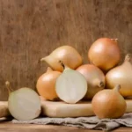 stack of white onions on wooden butcher's block with dark wood background