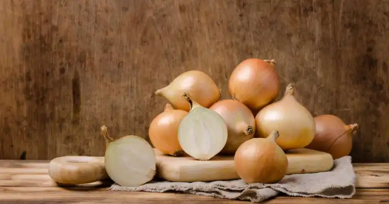 stack of white onions on wooden butcher's block with dark wood background