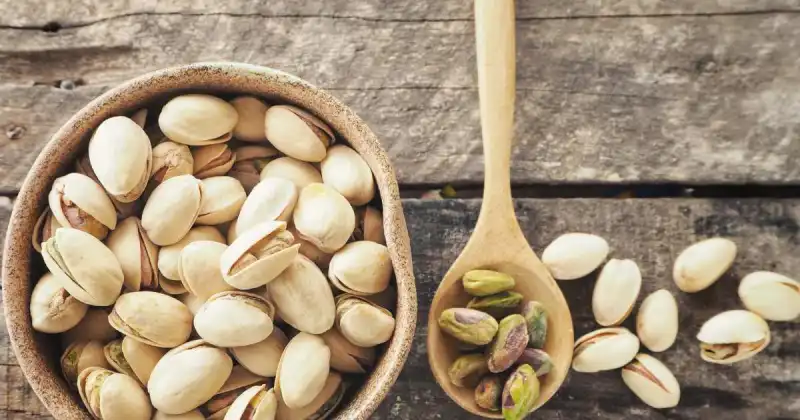 pistachios in small cup next to wooden spoon on dark wood table