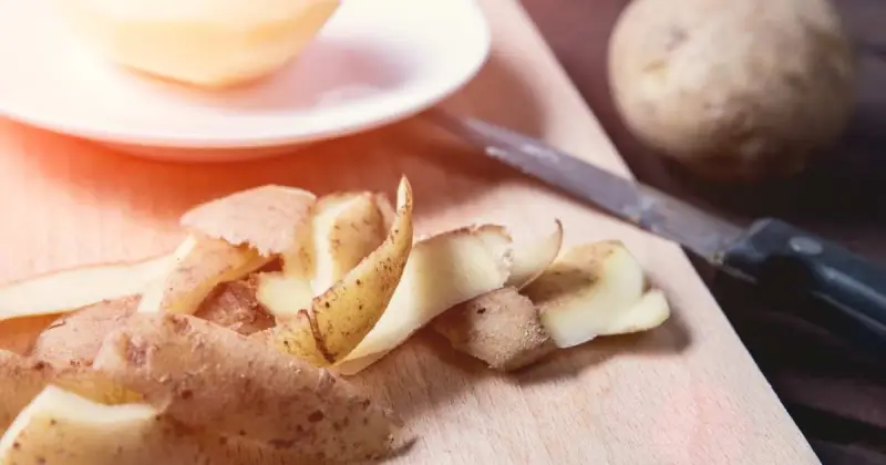 closeup of peeled potato skins on wooden cutting board near peeling knife