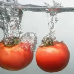side view of two ripe tomatoes dropping into clear water with bubbles
