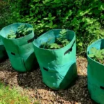 four large green grow bags filled with soil and young potato plants in outdoor garden with natural surroundings