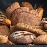 various loaves of bread and grains on wooden table with black background