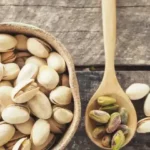 pistachios in small cup next to wooden spoon on dark wood table
