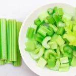 celery sticks on white table next to cut celery in white bowl