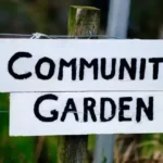 white and block community garden sign hanging on wooden post outside